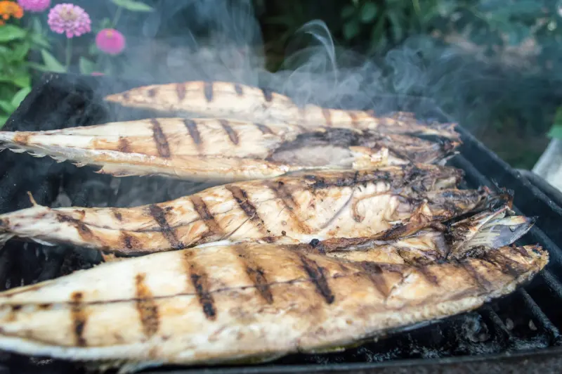 Peixes inteiros a grelhar sobre carvão, com marcas escuras da grelha.