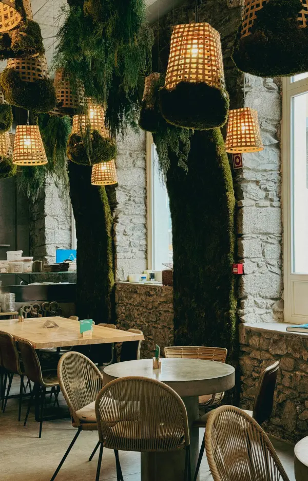 Sala de jantar com mesas de madeira, cadeiras de palhinha e candeeiros de verga pendurados.